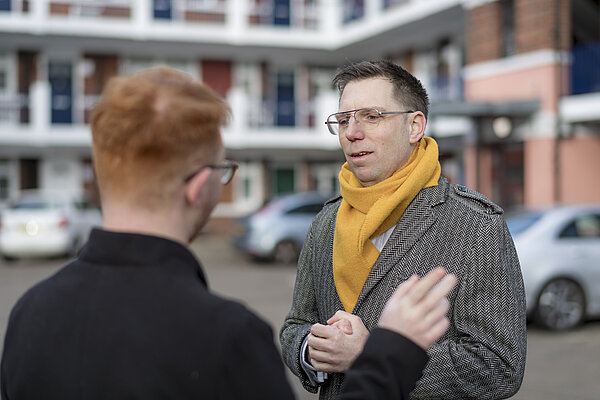 Rob Blackie wearing a yellow scarf, speaking to a resident on a housing estate
