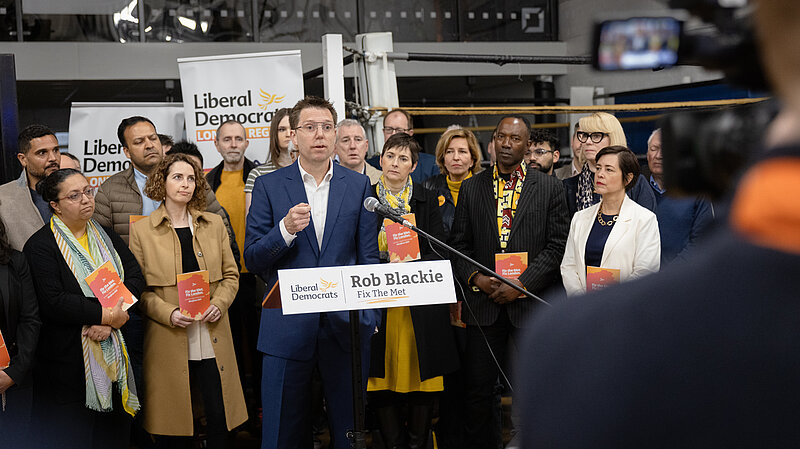 Rob Blackie pictured in a white shirt with a navy blazer. Lib Dem activists pictured behind. 